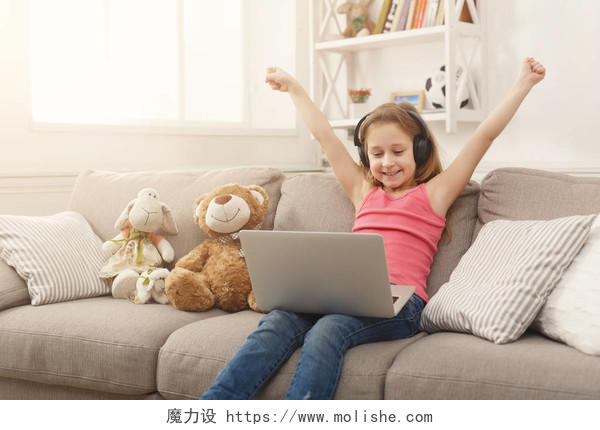 可爱的孩子带着耳机上玩笔记本电脑微笑的小女孩